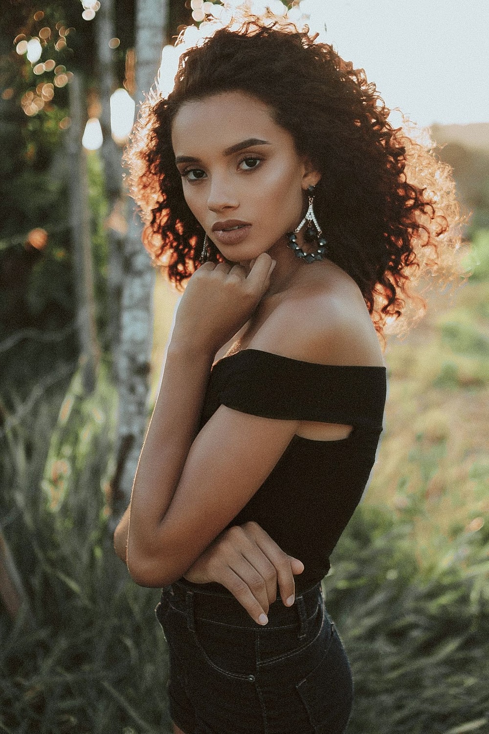 Woman posing outdoors with curly hair and earrings.