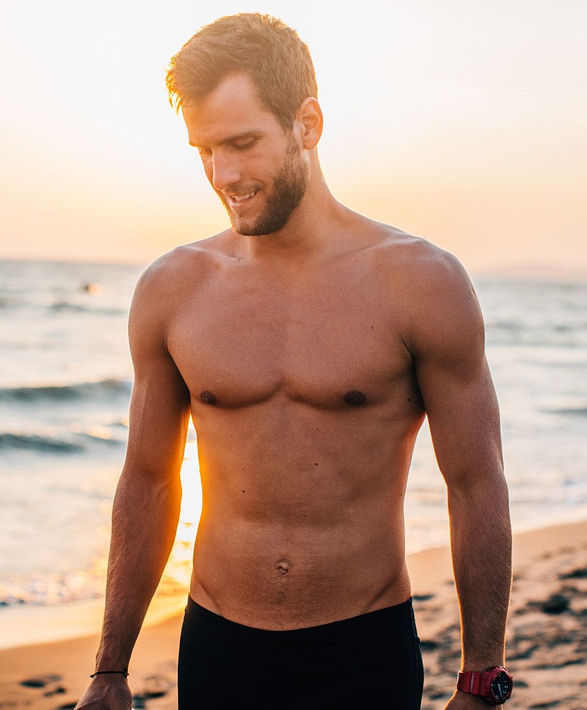 Man standing on beach at sunset, smiling.